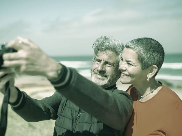A laughing couple with gray hair hiking together on a sunlit forest trail