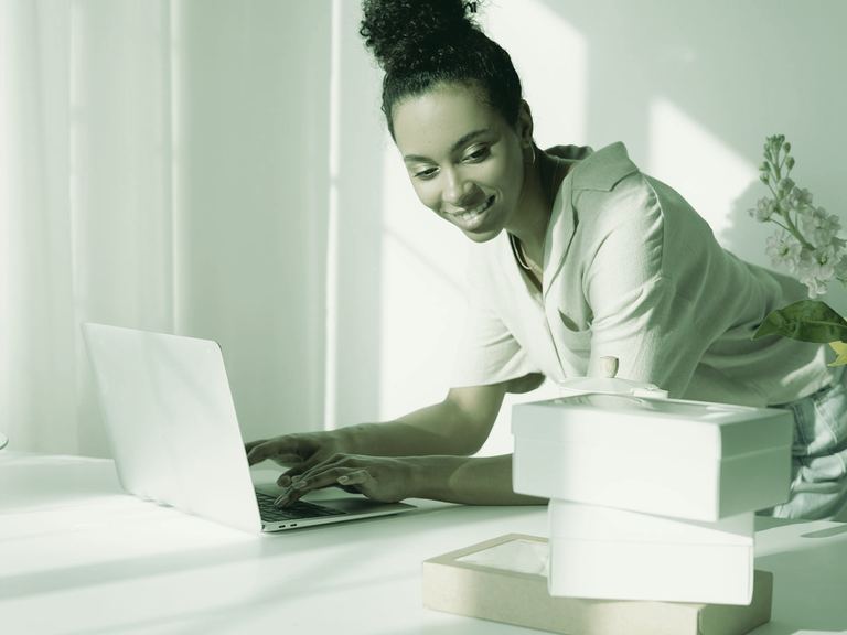 A smiling self-employed woman working on a laptop at a sunny kitchen table