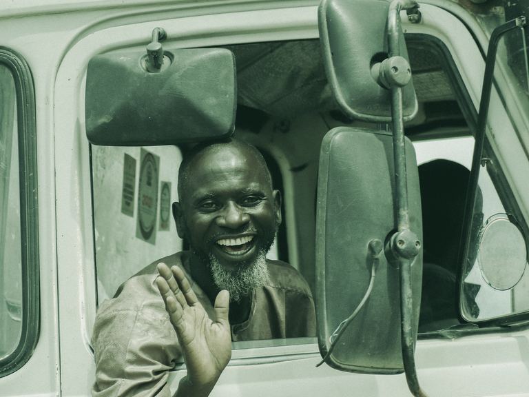 A smiling truck driver in a flannel shirt standing beside his semi truck at sunset